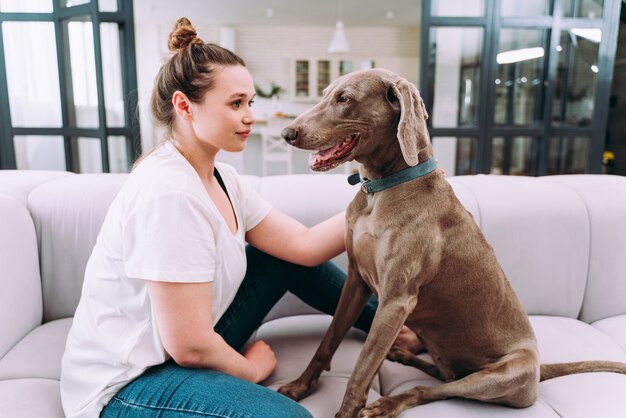 Moments de vie d'une jeune femme à la maison. Femme jouant avec son chien dans le salon