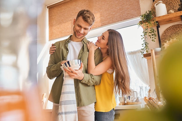 Mon amour. Un couple ravi et positif étant dans la cuisine et essuyant des bols propres après le petit-déjeuner