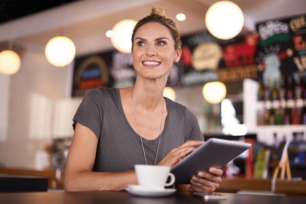 Mon application météo avait raison c'est une belle journée Une belle jeune femme utilisant sa tablette dans un café