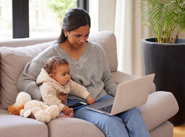 Mon contenu est tout au sujet de mon voyage de maternité. Photo d'une jeune femme travaillant sur son ordinateur portable assise dans le salon avec son bébé.