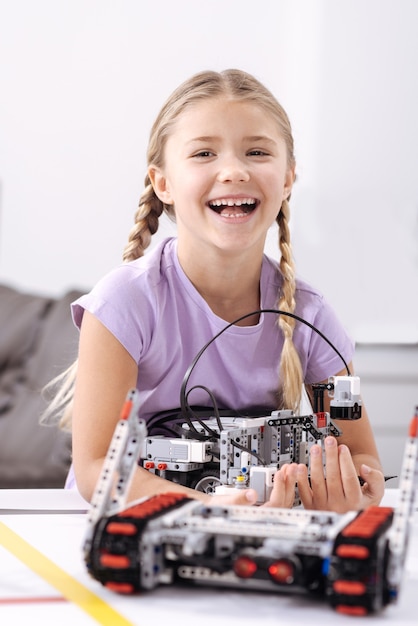 Mon Premier Projet Technologique. Joyeuse Fille Positive Heureuse Debout à L'école Et Tenant Un Robot électronique Tout En Exprimant Le Bonheur