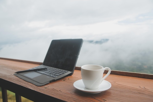 Moniteur d'ordinateur Clavier tasse à café et souris avec vide est sur la table de travail au ciel montagne rivière et arbres vue avant arrière-plan