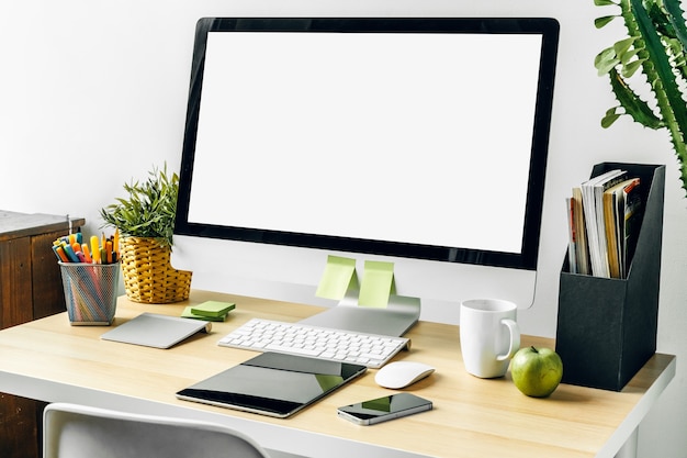 Moniteur d'ordinateur avec écran blanc maquette sur table de bureau avec fournitures