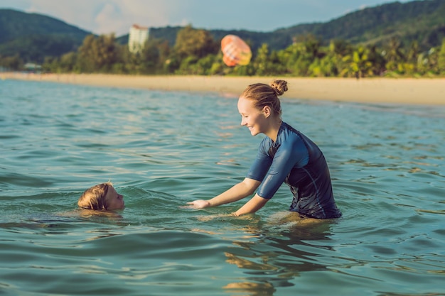 Une monitrice de natation pour enfants enseigne à un garçon heureux à nager dans la mer