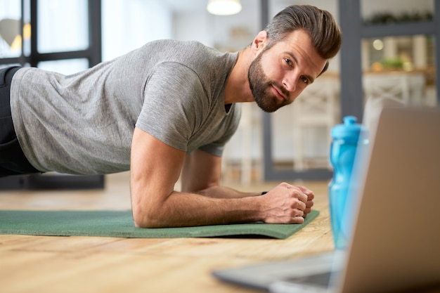 Monsieur barbu regardant un entraînement en ligne sur un ordinateur portable et faisant de l'exercice