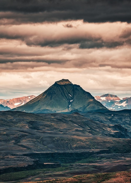 Montagne volcanique sur le champ de lave et ciel nuageux dans les hautes terres islandaises