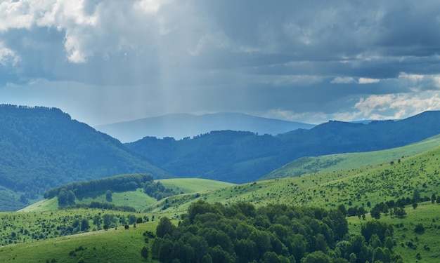 Montagnes et collines par temps orageux contrastant avec la verdure légère des forêts en été