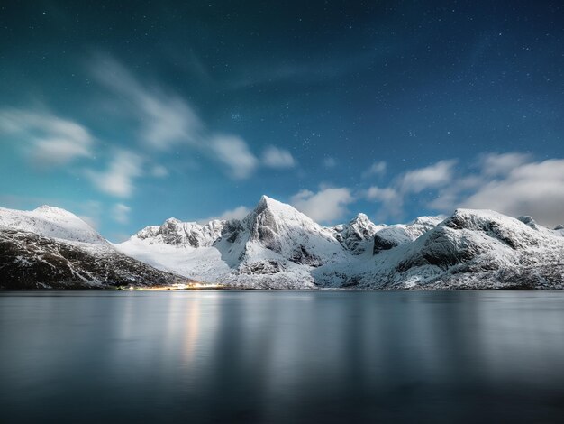 Photo des montagnes et des reflets sur l'eau la nuit paysage hivernal le ciel avec des étoiles et des nuages en mouvement la nature en arrière-plan voyage en norvège