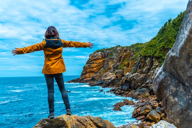 Monte Ulia dans la ville de San Sebastián, Pays Basque. Visitez la crique cachée de la ville appelée Illurgita Senadia ou Illurgita Senotia. Une jeune femme dans une veste jaune à bras ouverts