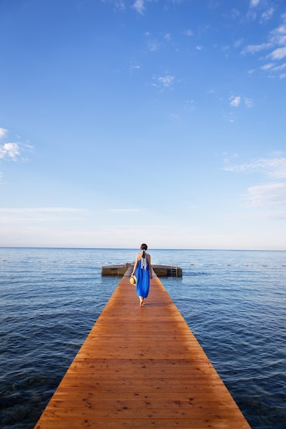 Monténégro Budva Fille dans une robe bleue se dresse sur une jetée en bois au bord de la mer beau ciel avec des nuages Concept de vacances voyage en Europe