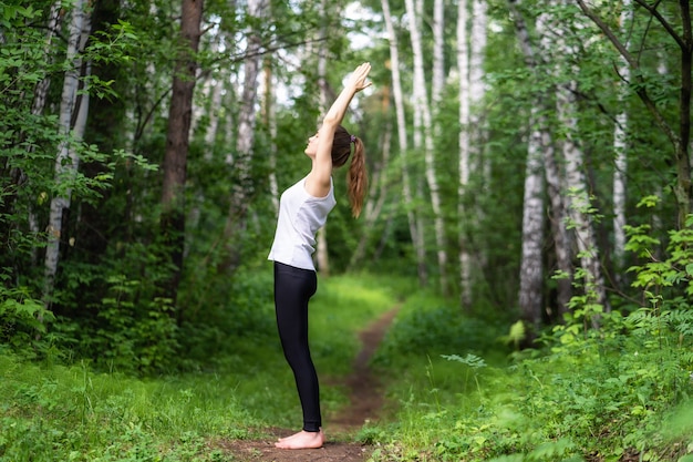 Monter la belle jeune femme portant haut blanc et leggings sportifs noirs travaillant à l'extérieur dans le parc le jour d'été.