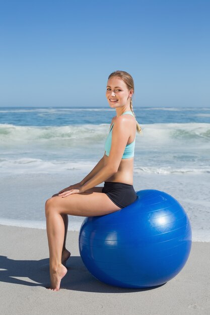 Monter la femme assise sur le ballon d&#39;exercice à la plage, souriant à la caméra