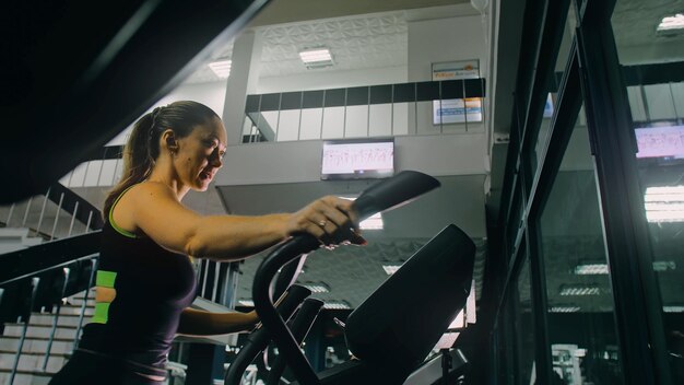 Monter une femme athlétique exerçant sur une machine elliptique, formation d'activité de femmes musclées dans un style moderne