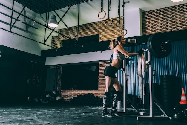 Photo monter une femme blonde au repos après l'entraînement soulevant un poids de barre dans la salle de sport