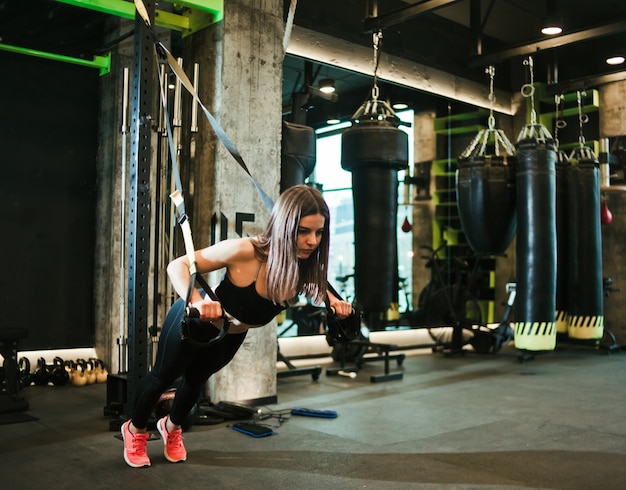 Monter la femme faisant de l'exercice avec une sangle de fitness au gymnase.