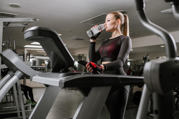 Monter la femme sur le tapis roulant avec une bouteille d'eau dans la salle de sport