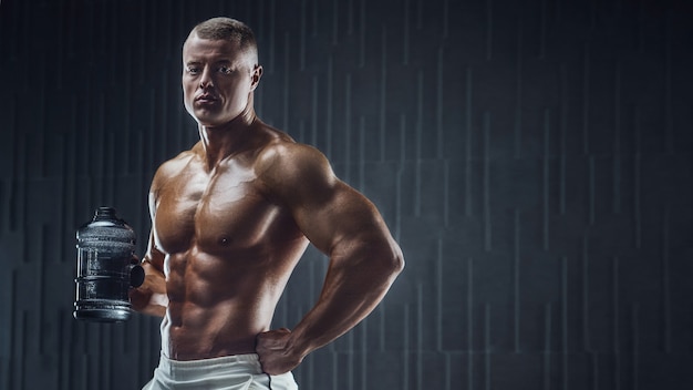 Monter l'homme à l'entraînement en salle de sport avec shaker sur fond sombre