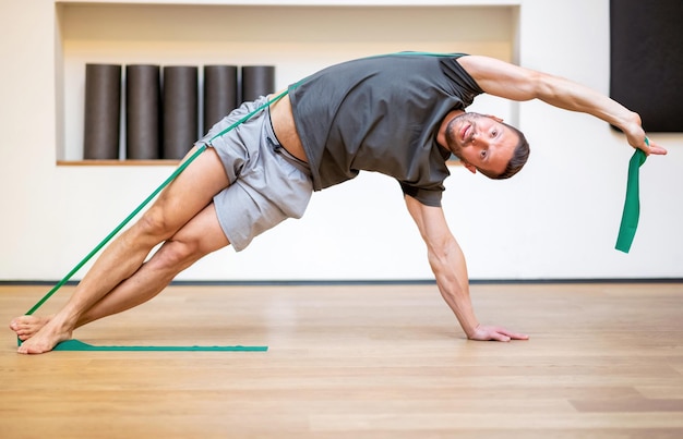 Monter un homme musclé faisant un exercice de bande de résistance dans un étirement latéral sur toute la longueur pour renforcer et tonifier ses muscles centraux