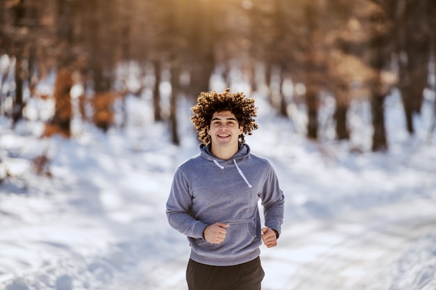 Monter l'homme de race blanche en tenue de sport et aux cheveux bouclés en cours d'exécution sur une route de campagne. L'hiver. Concept de fitness en plein air.