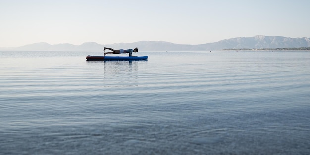 Monter la jeune femme faisant la position de la planche sur le plateau sup flottant sur l'eau de mer calme du matin