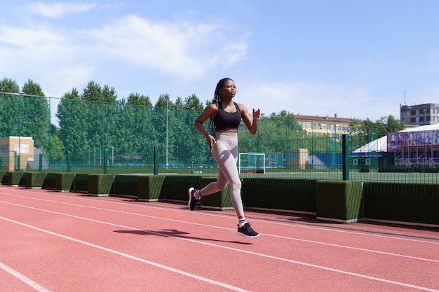 Monter la jeune femme noire en tenue de sport court sur la piste rouge du stade de la ville se préparant aux compétitions