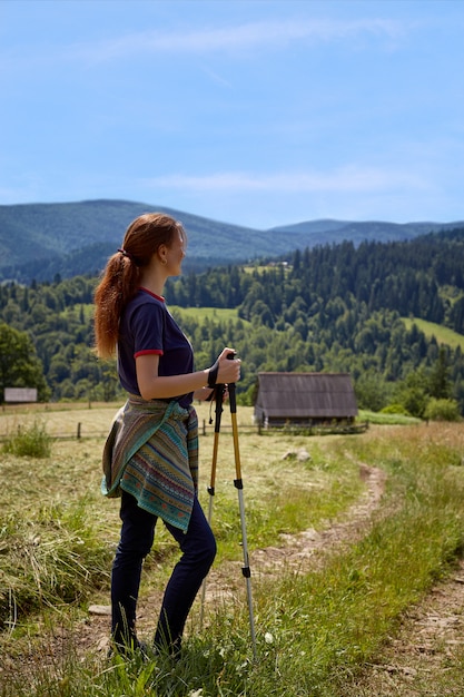 Monter jeune femme randonnée dans les montagnes debout sur une crête rocheuse avec sac à dos et poteau donnant sur un paysage alpin