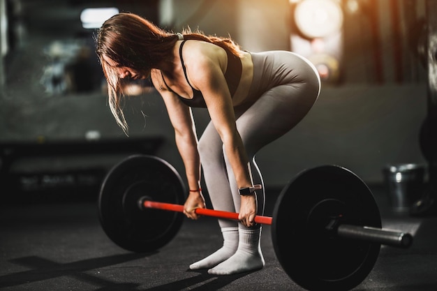 Monter la jeune femme travaillant à l'entraînement intensif dans la salle de sport. Elle fait des exercices de dos avec des haltères.