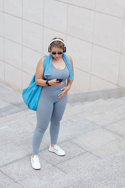 Monter une jeune sportive de taille plus dans des lunettes de soleil en choisissant de la musique pour s'entraîner sur un smartphone lorsqu'elle se tient à l'extérieur