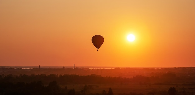 La montgolfière vole en vol libre au-dessus du champ Ballon multicolore dans le ciel au coucher du soleil