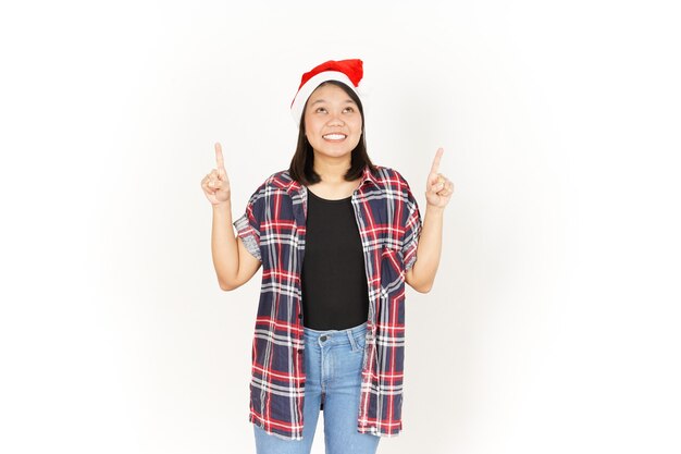 Montrant et pointant vers le haut d'une belle femme asiatique portant une chemise à carreaux rouge et un chapeau de Père Noël