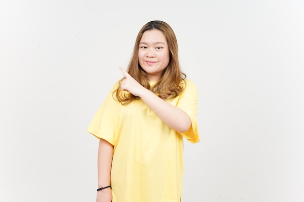 Montrant le produit et le côté pointant de la belle femme asiatique portant un t-shirt jaune isolé sur blanc