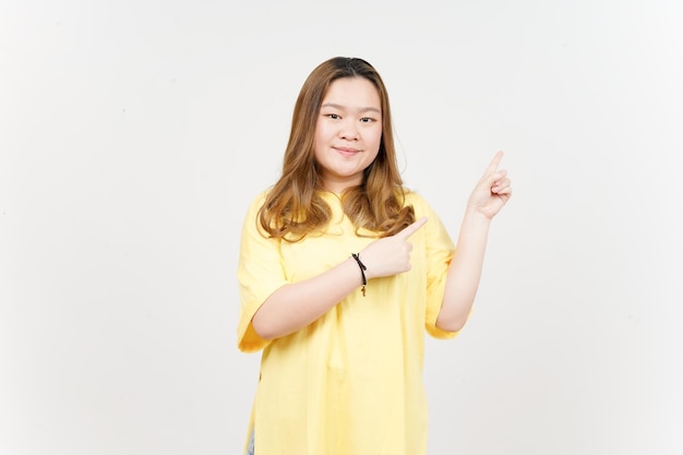 Montrant le produit et le côté pointant de la belle femme asiatique portant un t-shirt jaune isolé sur blanc