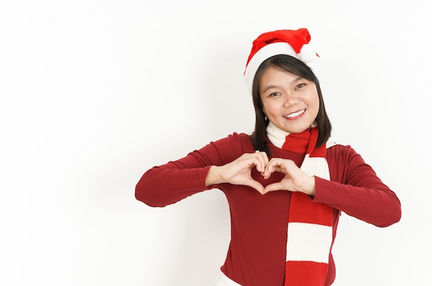 Montrant le signe du coeur de la belle femme asiatique portant un col roulé rouge et un bonnet de noel isolé sur blanc