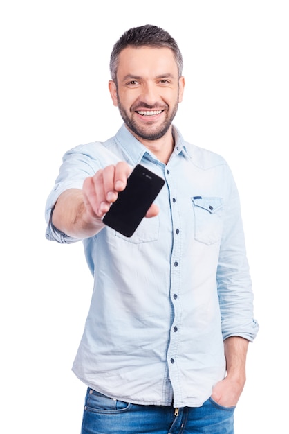 Montrant son tout nouveau téléphone intelligent. Beau jeune homme en tenue décontractée montrant son téléphone intelligent et souriant en se tenant debout isolé sur fond blanc