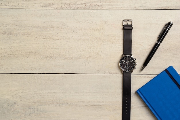 Une montre-bracelet mécanique, un agenda et un stylo se trouvent à droite sur une table en bois clair