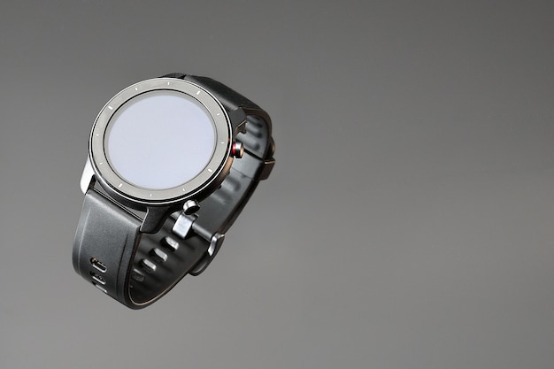 Photo montre intelligente sans fil dans un boîtier noir mat rond avec des risques sur la jante et un bracelet en silicone sur fond gris avec espace pour le texte.