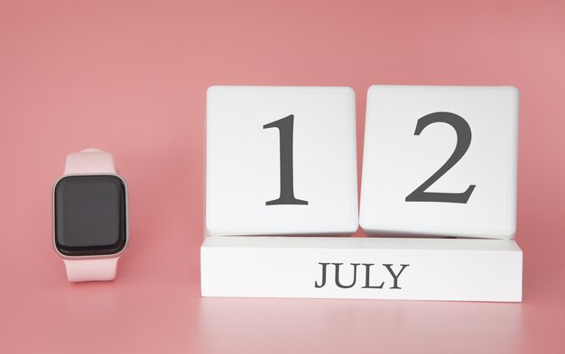 Montre moderne avec calendrier cube et date 12 juillet sur mur rose. Vacances d'été de concept.