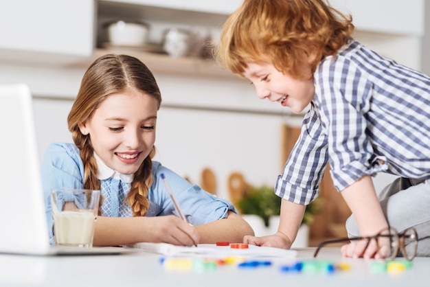 Montre-moi tes notes. Drôle charmant garçon aux cheveux rouges assis juste sur la table juste à côté de son frère et essayant de la faire plaisir tout en passant le week-end avec elle à la maison