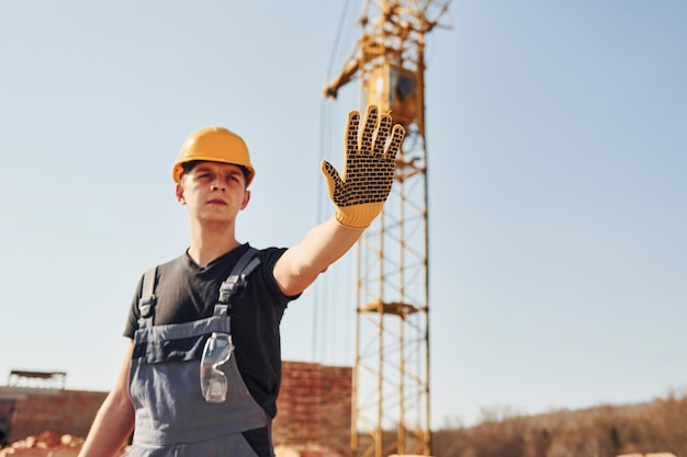 Montre le panneau d'arrêt à la main Un ouvrier du bâtiment en uniforme et équipement de sécurité a un travail sur le bâtiment