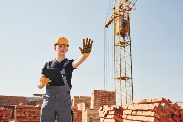 Montre le panneau d'arrêt à la main Un ouvrier du bâtiment en uniforme et équipement de sécurité a un travail sur le bâtiment