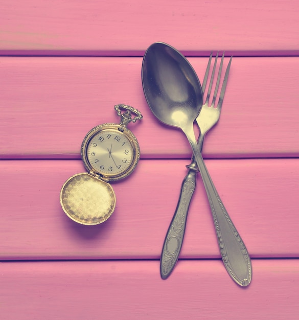 Montre de poche vintage, cuillère, fourchette sur une table en bois rose