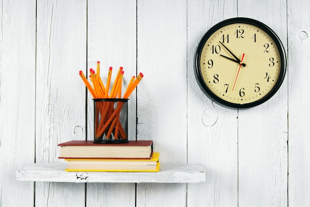 Montres, livres et outils scolaires sur une étagère en bois. Sur un fond en bois blanc.