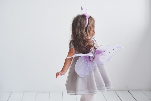 Montrez vos ailes. Jolie petite fille dans le costume de fée debout dans la chambre.