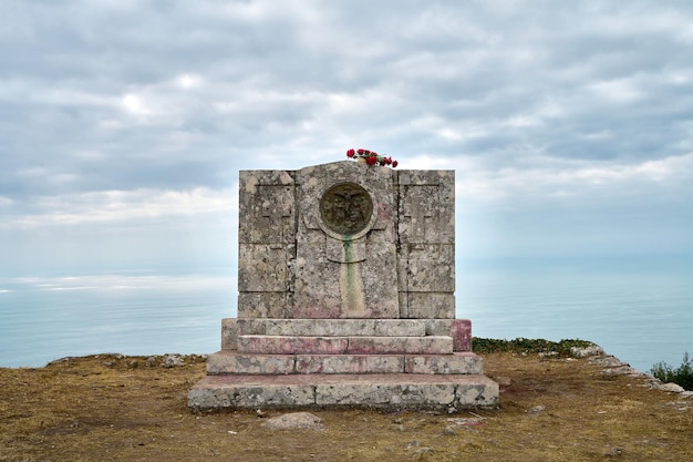 monument en pierre au sommet d'une montagne surplombant la mer par temps nuageux