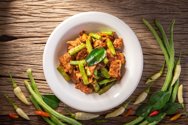 Moo Pad Prik Gaeng, cuisine thaïlandaise, porc sauté avec pâte de curry rouge, feuilles de bergamote et haricots verts sur fond de texture de bois naturel rustique, vue de dessus