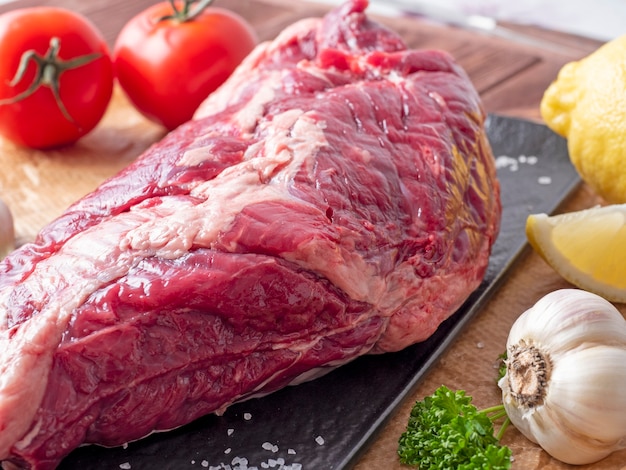 Un morceau de bœuf cru frais repose sur du parchemin entouré d'épices, d'herbes et de légumes. Vue de côté. Composition des aliments