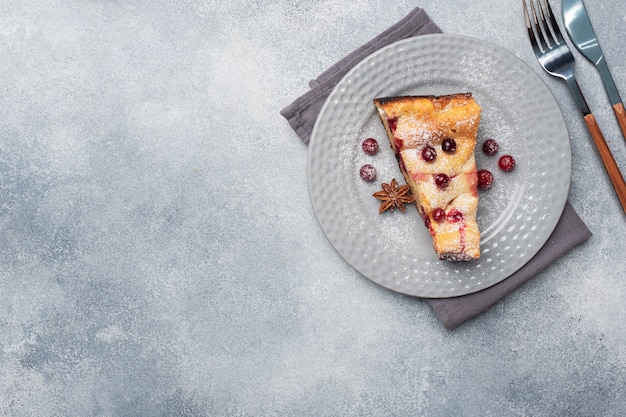 Un morceau de casserole de tarte au fromage cottage avec des canneberges et des épices cannelle et anis sur une assiette. Fond de béton gris. Copiez l'espace.