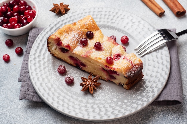 Un morceau de casserole de tarte au fromage cottage avec des canneberges et des épices cannelle et anis sur une assiette. Fond de béton gris.