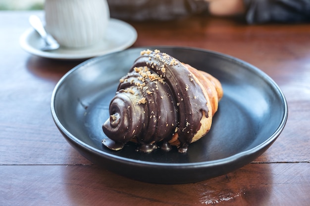 Un morceau de croissant au chocolat dans une assiette noire et une tasse de café sur une table en bois en boulangerie