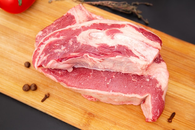 Morceau cru de steak de boeuf sur une planche à découper en bois avec des herbes et des épices. Ingrédients frais pour les restaurants. Viande sur l'os.